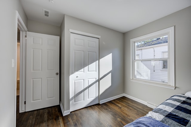 bedroom with a closet, dark wood-type flooring, and a baseboard heating unit