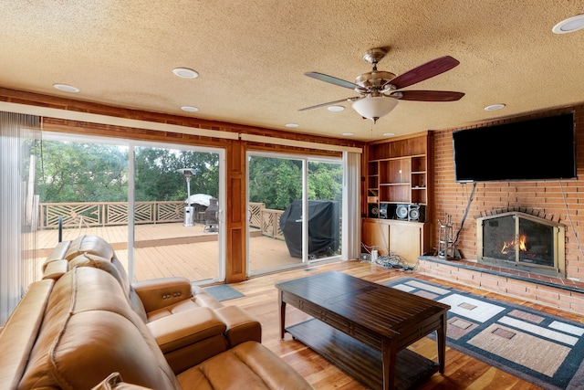 living room featuring a fireplace, a textured ceiling, light wood-type flooring, and ceiling fan