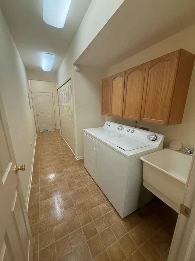 laundry area featuring washing machine and dryer, cabinet space, a sink, and baseboards