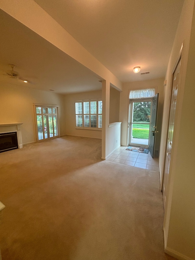 unfurnished living room featuring light carpet, light tile patterned flooring, visible vents, and a glass covered fireplace