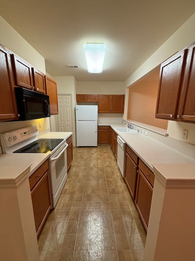 kitchen featuring brown cabinets, light countertops, visible vents, a sink, and white appliances