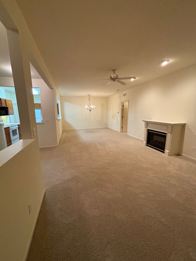 unfurnished living room featuring ceiling fan with notable chandelier, carpet floors, a glass covered fireplace, and baseboards