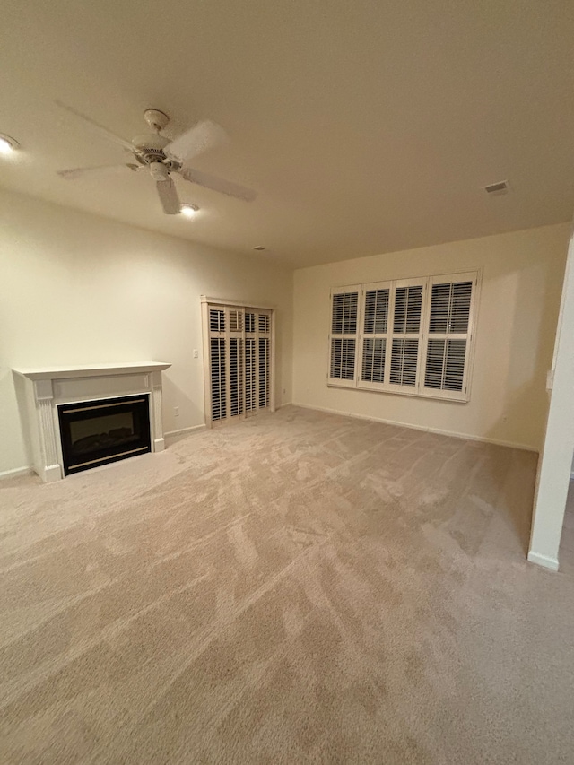 unfurnished living room featuring a glass covered fireplace, baseboards, ceiling fan, and carpet