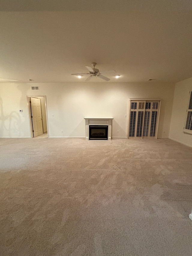 unfurnished living room featuring carpet, ceiling fan, a fireplace, and baseboards