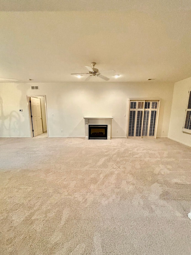 unfurnished living room with carpet floors, ceiling fan, a fireplace, and baseboards