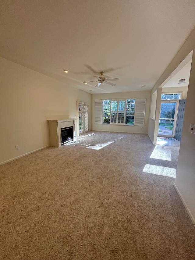 unfurnished living room featuring carpet, ceiling fan, a fireplace, and baseboards