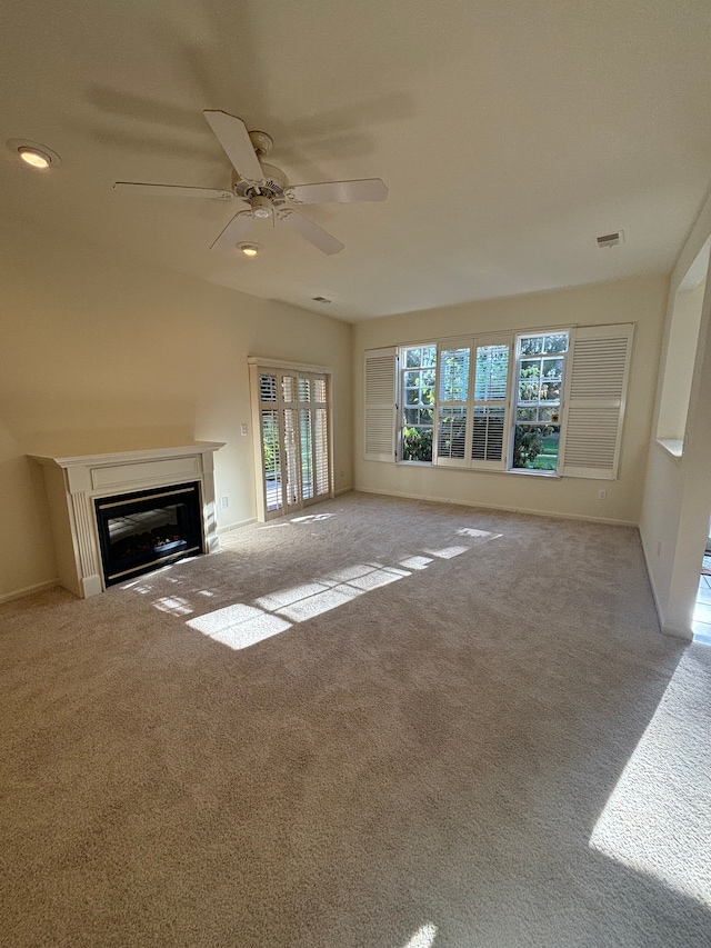 unfurnished living room featuring a glass covered fireplace, carpet flooring, visible vents, and a ceiling fan