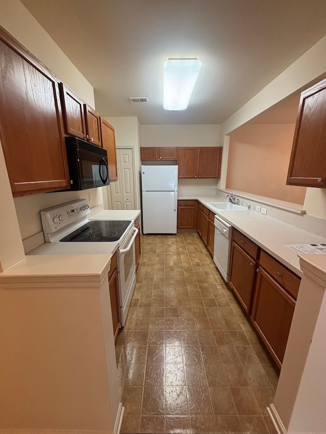 kitchen featuring white appliances, visible vents, brown cabinetry, and a sink