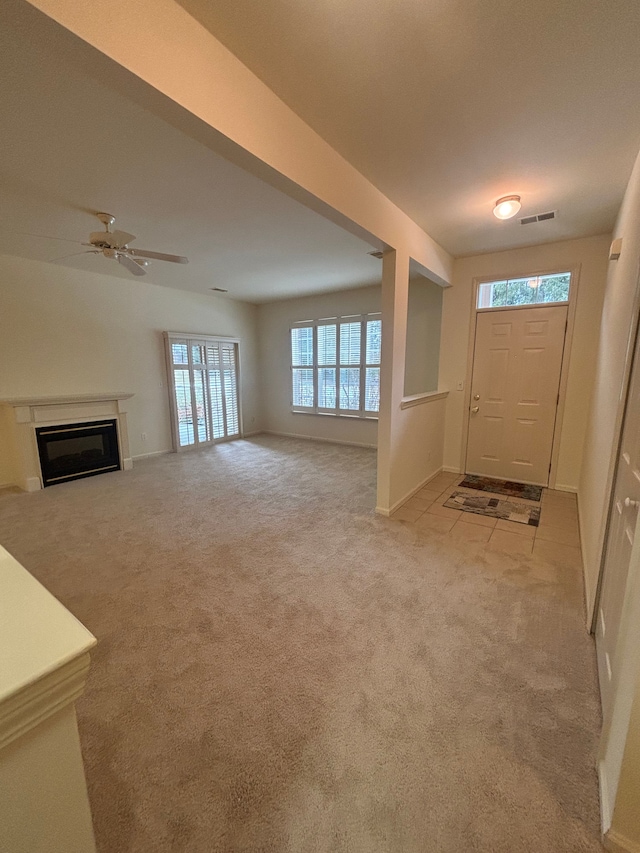 entryway with light colored carpet, visible vents, a glass covered fireplace, ceiling fan, and baseboards