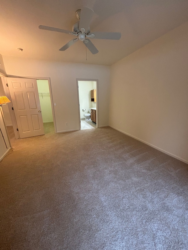 unfurnished bedroom with light carpet, a spacious closet, ensuite bath, and baseboards