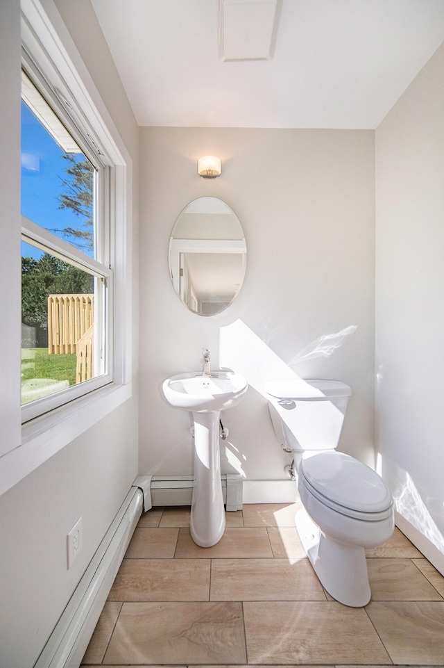 half bathroom with baseboards, wood finish floors, a baseboard radiator, a sink, and toilet