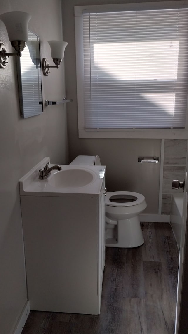 bathroom featuring hardwood / wood-style flooring, vanity, toilet, and a tub to relax in