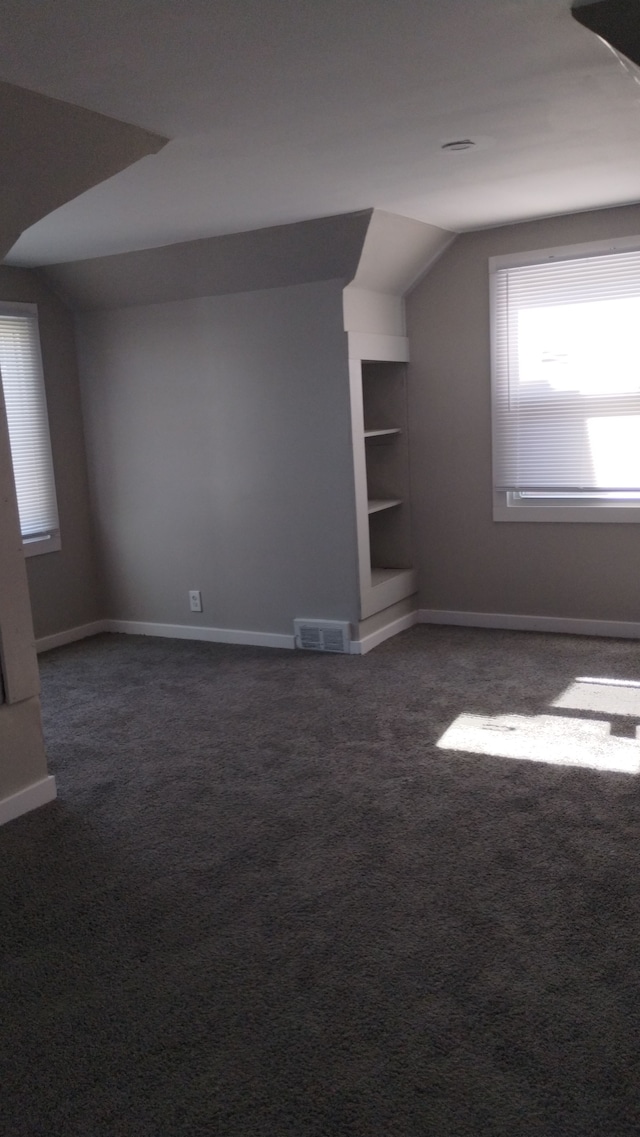 bonus room with lofted ceiling, dark carpet, and built in features