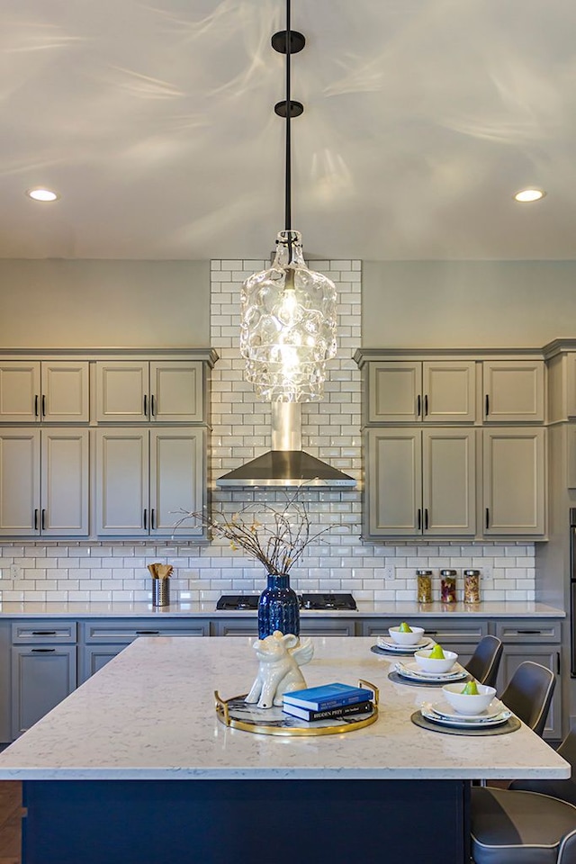 kitchen featuring stainless steel gas stovetop, wall chimney range hood, hanging light fixtures, decorative backsplash, and a kitchen island