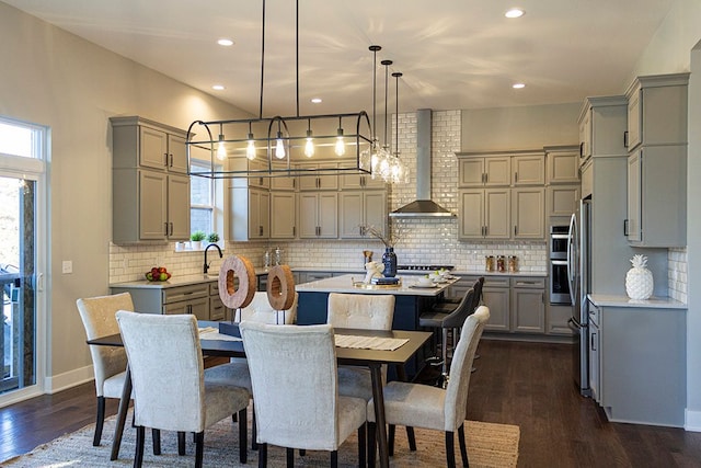 kitchen with gray cabinetry, a center island, wall chimney exhaust hood, dark hardwood / wood-style flooring, and pendant lighting