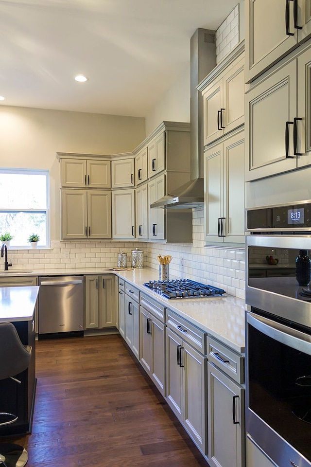 kitchen featuring decorative backsplash, appliances with stainless steel finishes, dark hardwood / wood-style flooring, and wall chimney exhaust hood