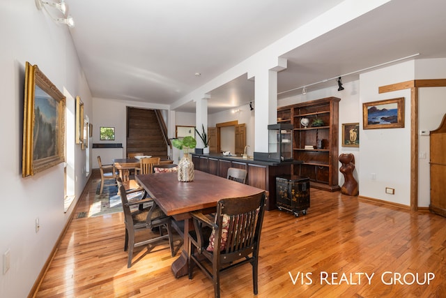 dining space with light hardwood / wood-style floors, track lighting, and sink