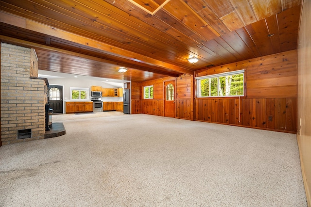 unfurnished living room with carpet, wood ceiling, a healthy amount of sunlight, and wood walls