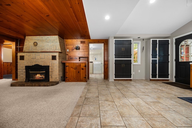 unfurnished living room featuring light carpet, vaulted ceiling, a fireplace, washer / dryer, and wood walls