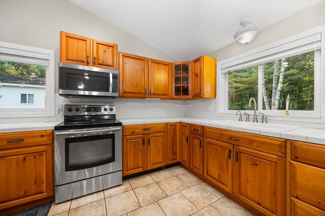 1758 W Nestel Rd, Prudenville, MI 48651 - kitchen with appliances with stainless steel finishes, vaulted ceiling, decorative backsplash, and brown cabinets