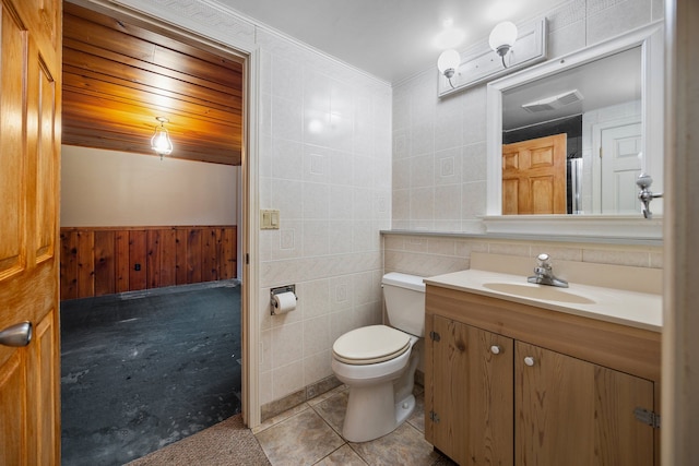 bathroom featuring tile patterned flooring, wood walls, toilet, vanity, and tile walls