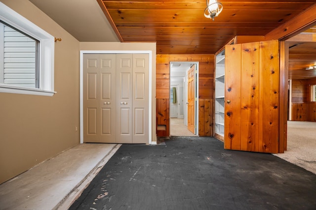 unfurnished bedroom featuring dark colored carpet, wood ceiling, wooden walls, and a closet