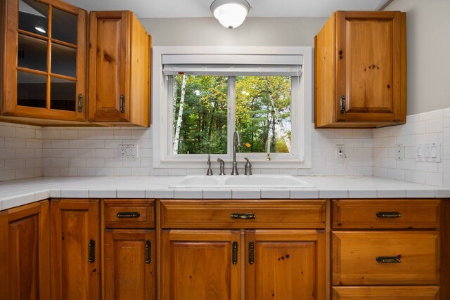 1758 W Nestel Rd, Prudenville, MI 48651 - kitchen with a sink, brown cabinets, glass insert cabinets, and tasteful backsplash