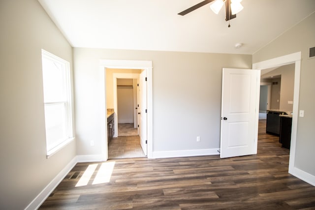 unfurnished bedroom featuring ceiling fan, ensuite bathroom, dark wood-type flooring, and lofted ceiling