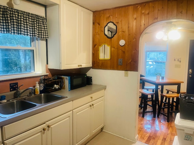 kitchen featuring wood walls, white cabinets, sink, ceiling fan, and light hardwood / wood-style floors