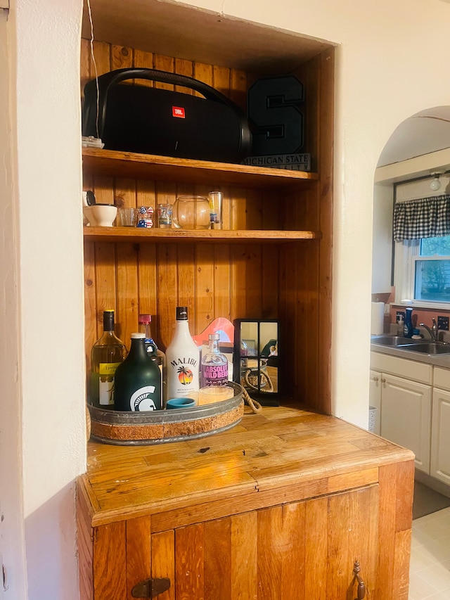 bar with sink, light tile patterned floors, and wood counters