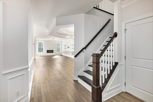 staircase with a fireplace, ornamental molding, hardwood / wood-style flooring, and a tray ceiling