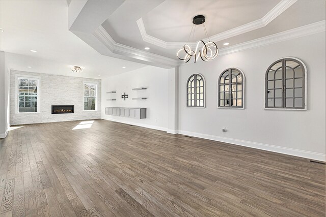 unfurnished living room with dark wood-type flooring, an inviting chandelier, a raised ceiling, crown molding, and a fireplace