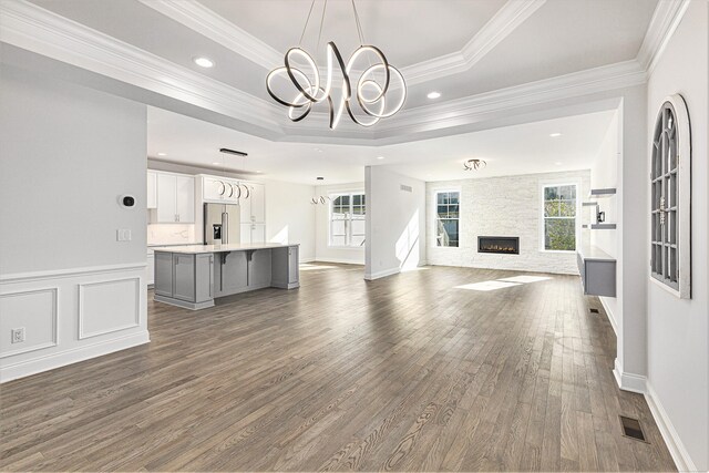 unfurnished living room with dark hardwood / wood-style floors, plenty of natural light, ornamental molding, and a tray ceiling