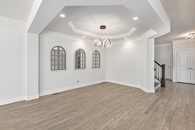 empty room featuring a raised ceiling, ornamental molding, light hardwood / wood-style floors, and an inviting chandelier