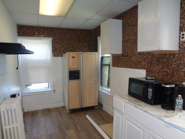 kitchen featuring light wood-type flooring, tasteful backsplash, a drop ceiling, radiator, and white cabinets