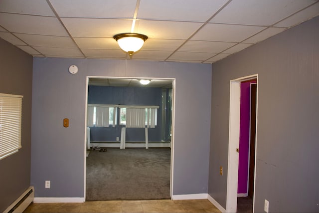 unfurnished room featuring tile patterned flooring, a drop ceiling, and a baseboard heating unit