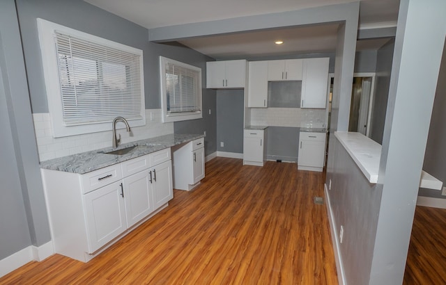 kitchen with white cabinetry, wood-type flooring, sink, and backsplash