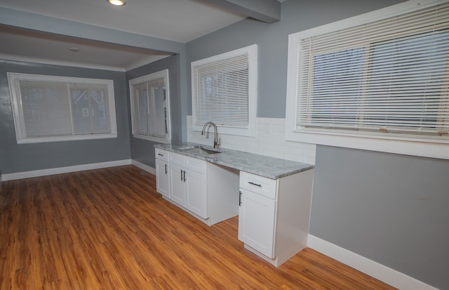 kitchen with white cabinetry, sink, backsplash, light stone counters, and light hardwood / wood-style flooring