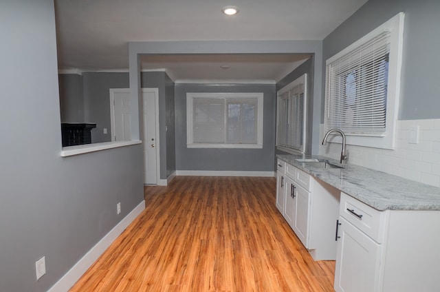 kitchen with sink, white cabinetry, light stone counters, light hardwood / wood-style floors, and decorative backsplash