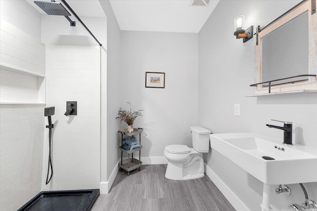 bathroom featuring sink, toilet, wood-type flooring, and tiled shower