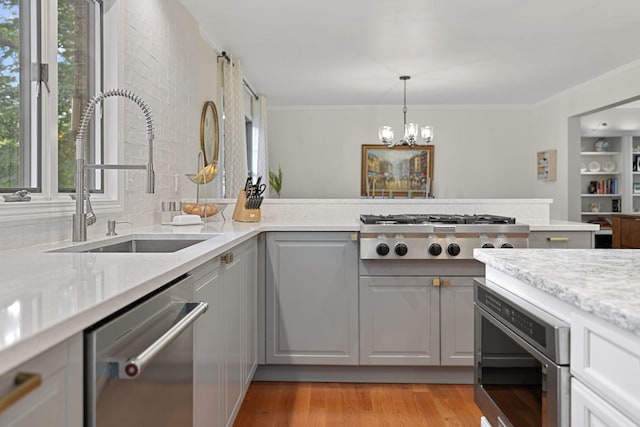 kitchen with appliances with stainless steel finishes, sink, gray cabinets, a notable chandelier, and light hardwood / wood-style floors