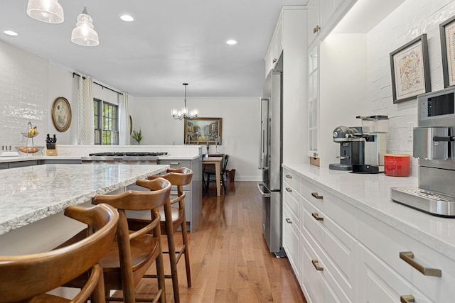 kitchen with light stone countertops, white cabinetry, pendant lighting, light hardwood / wood-style floors, and a breakfast bar