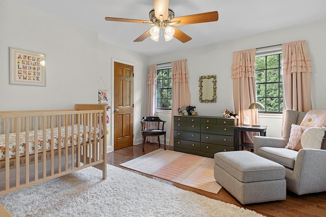 bedroom with ceiling fan, wood-type flooring, and a crib