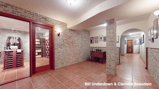 hallway with brick wall, tile patterned floors, and a textured ceiling