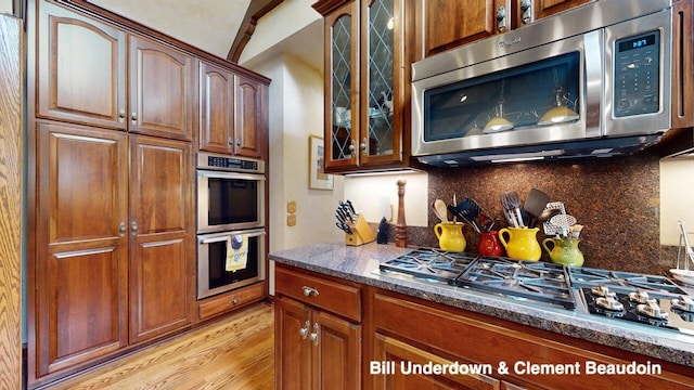 kitchen featuring dark stone countertops, tasteful backsplash, light hardwood / wood-style floors, and appliances with stainless steel finishes