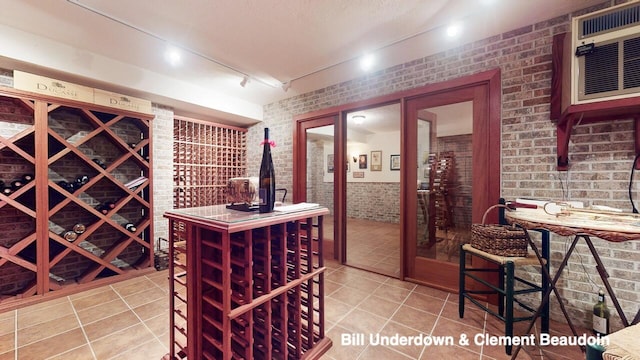 wine room featuring light tile patterned floors, a wall unit AC, rail lighting, and brick wall