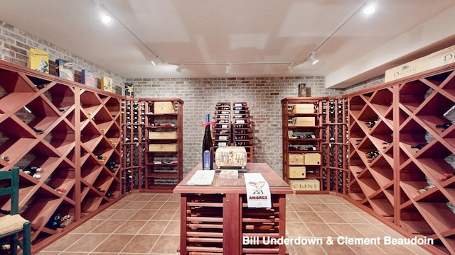 wine area with tile patterned floors, brick wall, and track lighting