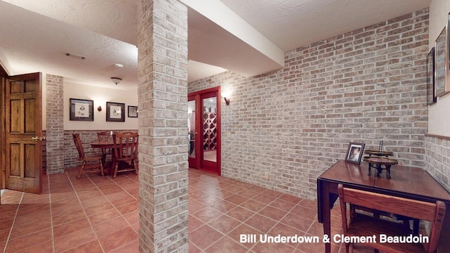 hallway featuring decorative columns, brick wall, and tile patterned flooring