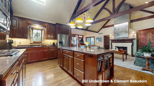 kitchen with hanging light fixtures, appliances with stainless steel finishes, a kitchen island, beamed ceiling, and light hardwood / wood-style floors