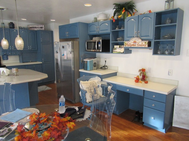 kitchen with pendant lighting, dark hardwood / wood-style floors, built in desk, blue cabinetry, and stainless steel appliances